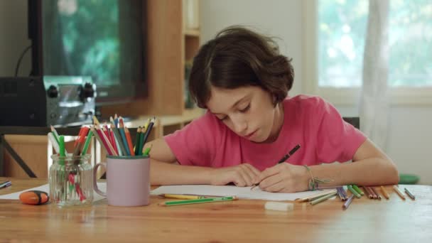 Молода дівчина сидить за столом малює кольоровими олівцями — стокове відео