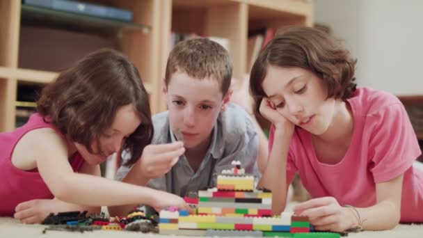 Drei Kinder spielen zu Hause mit Legosteinen — Stockvideo