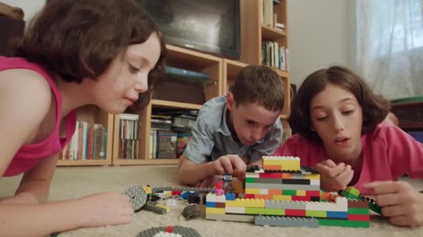 Três crianças brincando com tijolos de lego em casa — Vídeo de Stock