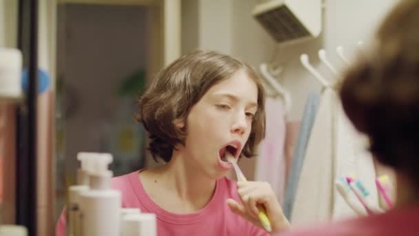 Ung flicka borsta hennes tänder framför spegeln — Stockvideo
