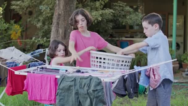 Tres niños quitando la ropa de la línea colgante a la cesta — Vídeos de Stock