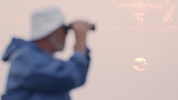 Старый рыбак смотрит в океан, используя бинокль — стоковое видео