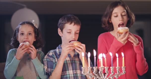 Crianças e sua mãe comendo donuts com uma menora e dreidels — Vídeo de Stock