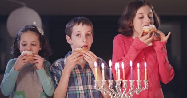 Crianças e sua mãe comendo donuts com uma menora e dreidels — Vídeo de Stock