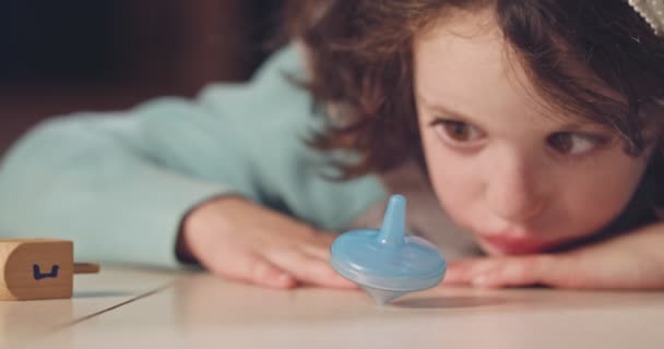 Nära upp skott av en flicka som snurrar en Hanukka dreidel på golvet — Stockvideo