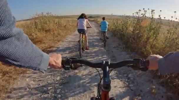 POV de duas crianças desfrutando de um passeio de bicicleta no campo com seu pai — Vídeo de Stock