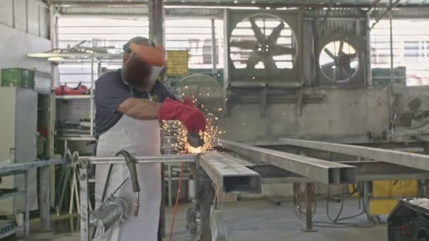 Movimiento lento de un trabajador que utiliza una amoladora de metal con chispas volando en una tienda de metal — Vídeos de Stock