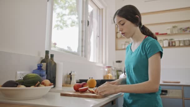 Gadis remaja bekerja memotong buah untuk sarapan di dapur — Stok Video