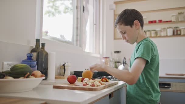 Ung pojke som arbetar i köket skivning frukt till frukost — Stockvideo