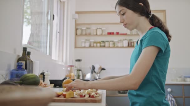 Tonårstjej som skär frukt till frukost i köket — Stockvideo