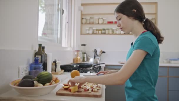 Дівчинка-підліток працює над розрізанням фруктів на сніданок на кухні — стокове відео