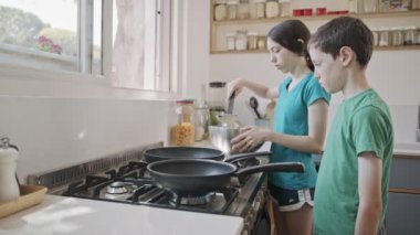 Küçük çocuklar mutfakta kızartma tavası kullanarak krep hazırlıyorlar.