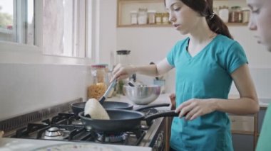 Küçük çocuklar mutfakta kızartma tavası kullanarak krep hazırlıyorlar.