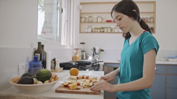 Adolescente trabalhando cortando frutas para o café da manhã na cozinha — Vídeo de Stock