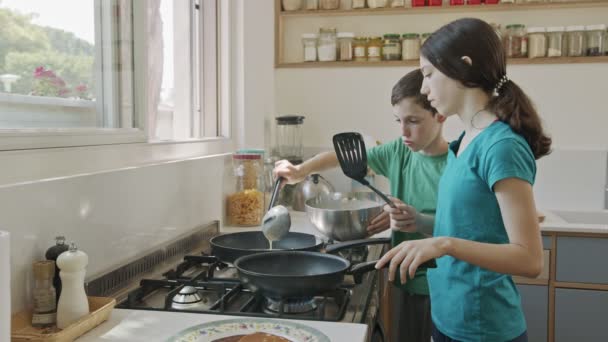 Küçük çocuklar mutfakta kızartma tavası kullanarak krep hazırlıyorlar. — Stok video