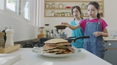 İki genç kız mutfakta tavayla krep hazırlıyor.