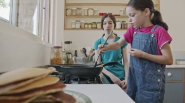 İki genç kız mutfakta tavayla krep hazırlıyor.