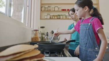 İki genç kız mutfakta tavayla krep hazırlıyor.