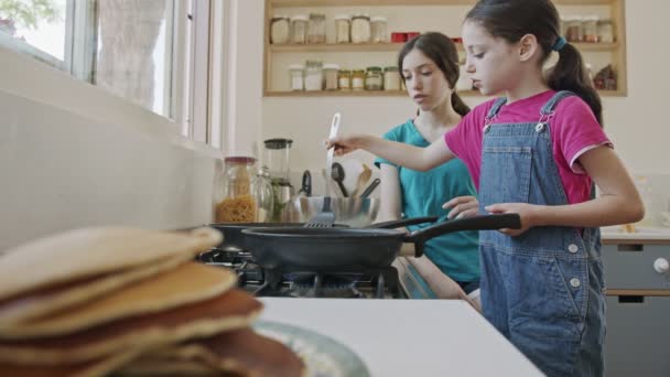 Dos chicas jóvenes preparando panqueques en la cocina usando una sartén — Vídeo de stock