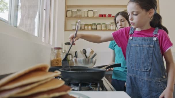 Dua gadis muda menyiapkan pancake di dapur menggunakan penggorengan — Stok Video