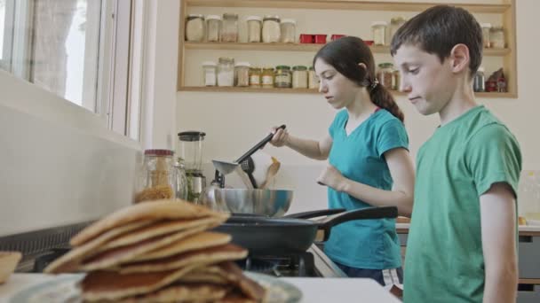 Küçük çocuklar mutfakta kızartma tavası kullanarak krep hazırlıyorlar. — Stok video