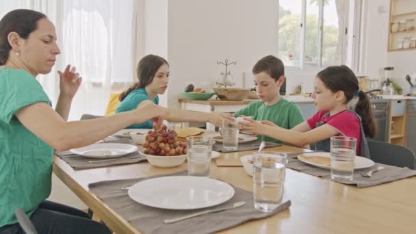 Mor och tre barn äter frukost av pannkakor och frukter — Stockvideo