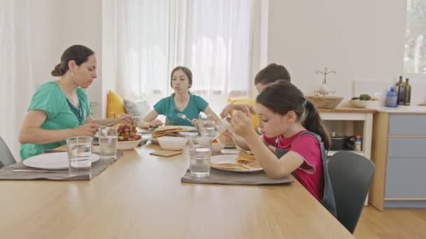 Moeder en drie kinderen ontbijten van pannenkoeken en fruit — Stockvideo