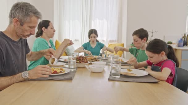 Familj på fem personer som sitter vid bordet och äter pannkakor och frukter till frukost — Stockvideo