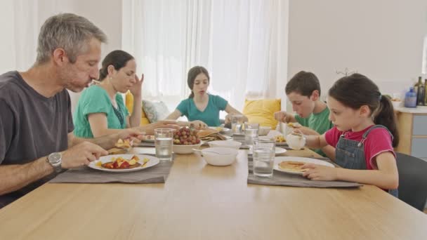 Trois enfants prennent le petit déjeuner de crêpes et de fruits avec leurs parents — Video