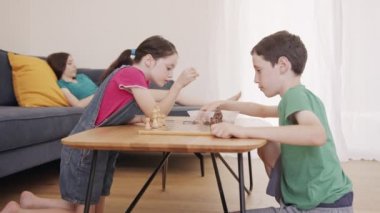 Çocuklar oturma odasındaki masada satranç oynuyorlar.