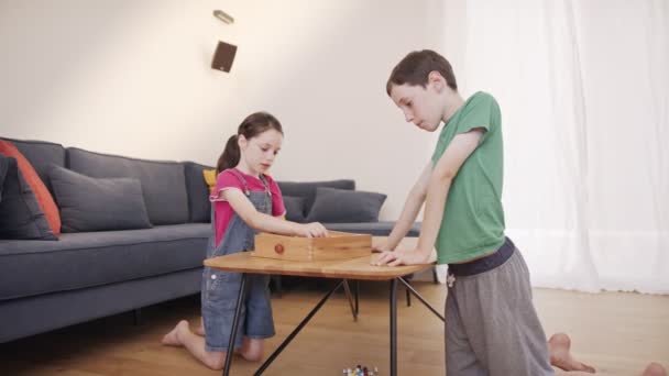 Jongen en meisje spelen een houten tafel spel in de woonkamer samen — Stockvideo