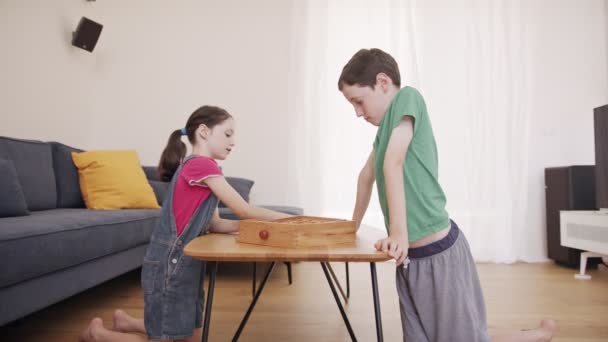 Pojke och flicka spelar ett träbord spel i vardagsrummet tillsammans — Stockvideo