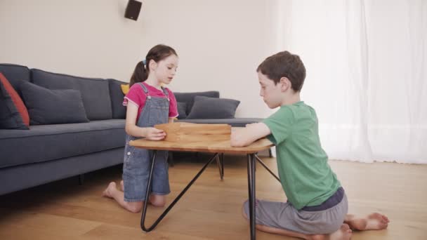 男の子と女の子が一緒にリビングルームで木製のテーブルゲームをプレイ — ストック動画