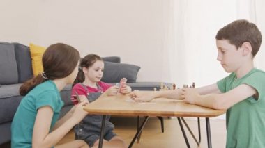 Oturma odasında beşik oyunu oynayan üç çocuk, bağırıyor ve tartışıyor.