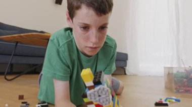 Genç bir çocuk oturma odasının zemininde oyuncak tuğlalarla oynuyor ve inşa ediyor.