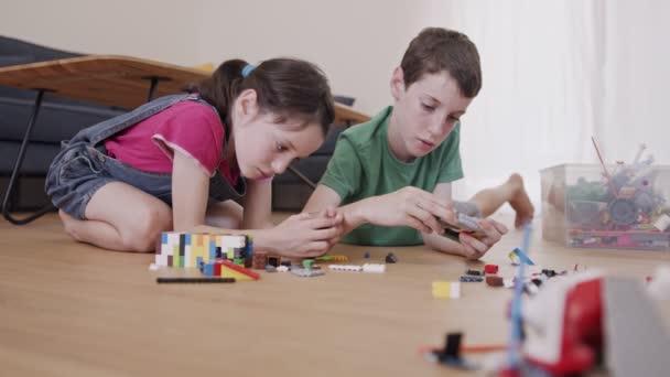 Mädchen und ein Junge spielen und bauen mit Spielzeugsteinen auf dem Wohnzimmerboden — Stockvideo