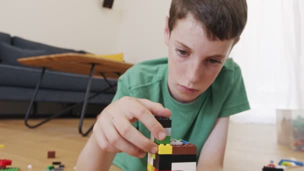 Młody chłopiec bawiący się i budujący cegłami zabawek na podłodze w salonie — Wideo stockowe