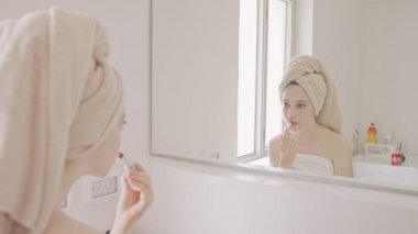 Genç kız banyo aynasının önünde makyaj yapıyor.