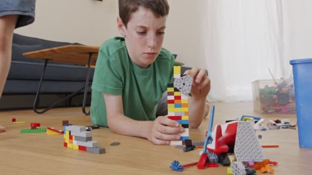 Giovane ragazzo che gioca e costruisce con mattoni giocattolo sul pavimento del soggiorno — Video Stock