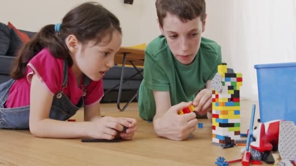 Ragazza e un ragazzo che giocano e costruiscono con mattoni giocattolo sul pavimento del soggiorno — Video Stock