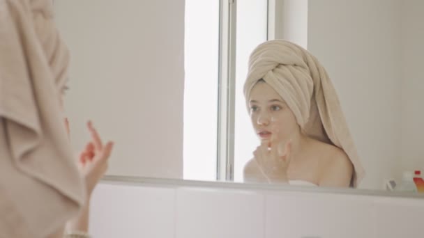 Genç kız banyodaki aynaya bakıyor - yüzünü kontrol ediyor. — Stok video