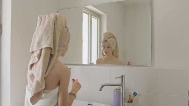 Дівчина-підліток наносить туш перед дзеркалом у ванній — стокове відео