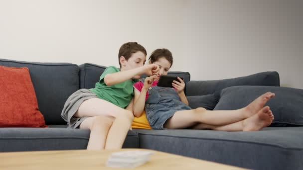 집에 있는 큰 소파에 앉아 핸드폰을 사용하는 두 아이 — 비디오