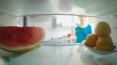 POV, bir buzdolabının içinde kapıyı açan ve yiyecekleri alan bir kadının fotoğrafını çekti.