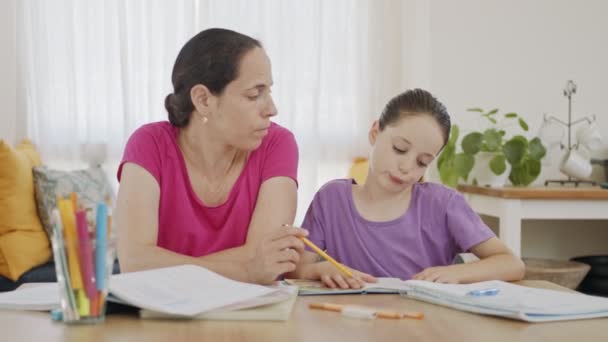 Мама помогает своей маленькой дочери подготовить домашнее задание во время домашнего обучения — стоковое видео