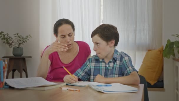 Мама помогает своему маленькому сыну подготовить домашнее задание во время домашнего обучения — стоковое видео
