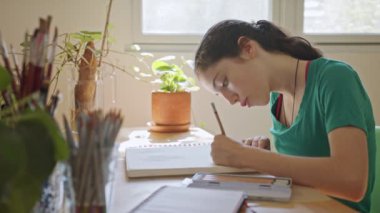 Genç ressam odasında bir eskiz defterine resim çiziyor.