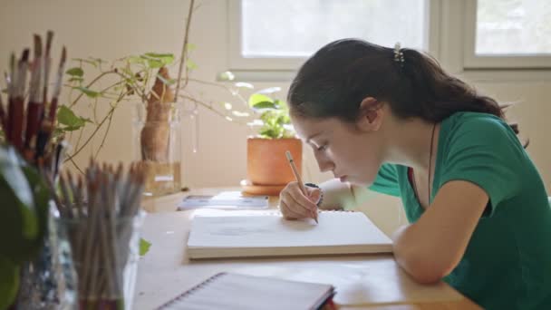 Teenager-Künstlerin sitzt Zeichnung in einem Skizzenbuch in ihrem Zimmer — Stockvideo