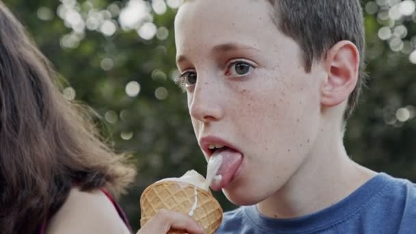 Fiatal fiú eszik fagylaltot egy kúp, élvezi és nevet — Stock videók