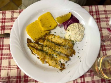 Ekose masa örtüsü üzerine kızarmış balık, limon dilimi ve tartar sosu..